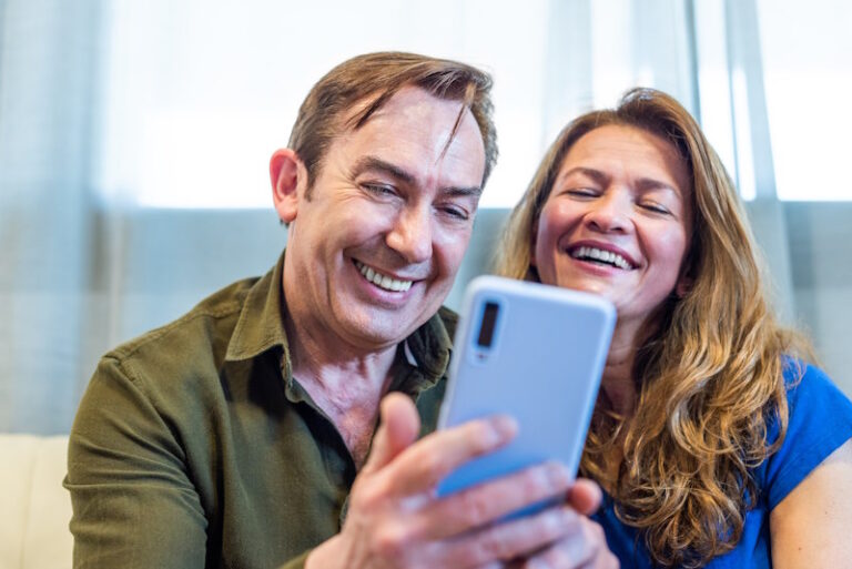 Smiling mature couple at home watching something funny on mobile. High quality photo