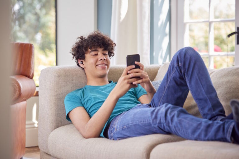 Teenage Boy Lying On Sofa At Home Using Mobile Phone